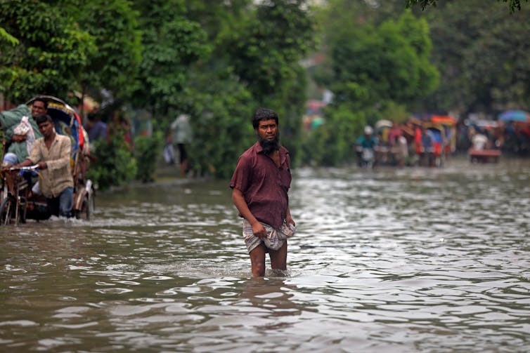 A man stands in a street flooded with water.